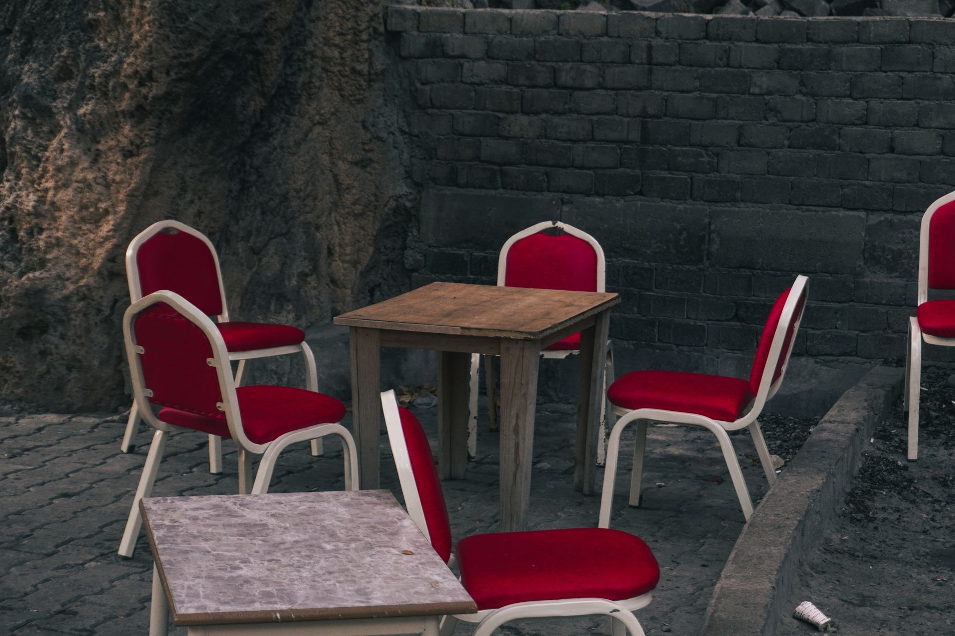 Empty outdoor seating area with red chairs and a wooden table against a brick wall.