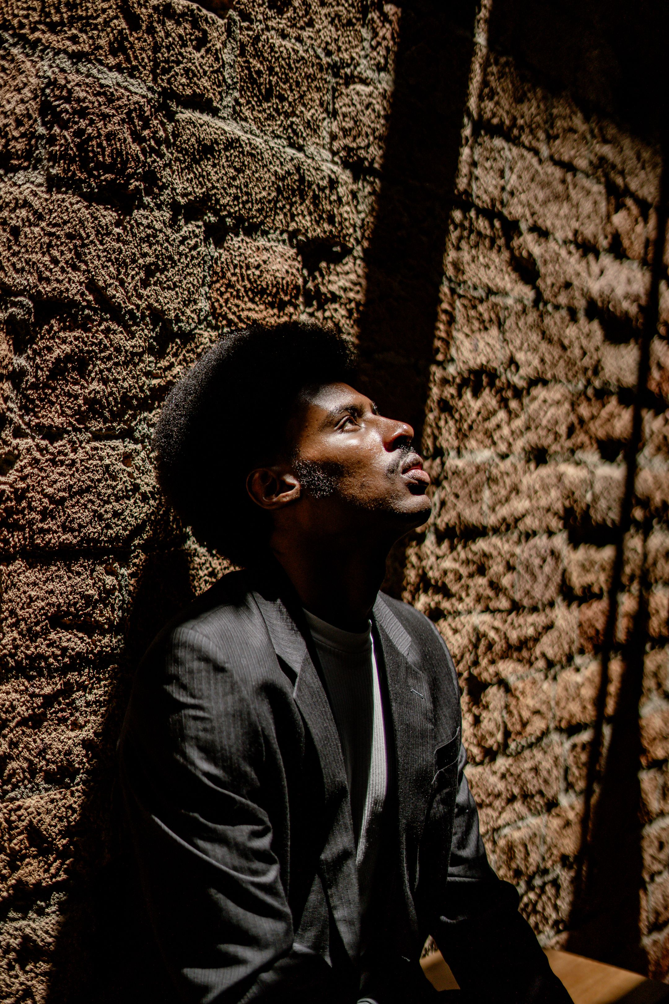 A thoughtful man in a suit looks contemplative against a textured brick wall.