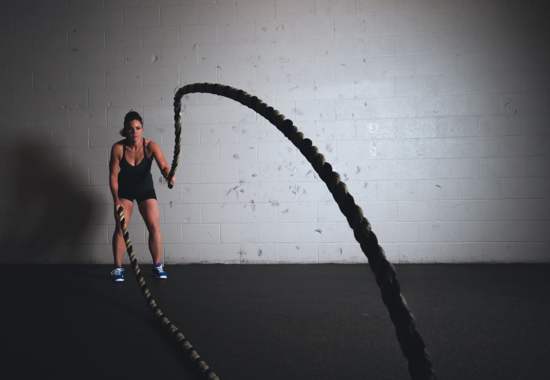 A focused woman performs a dynamic battle rope exercise in a gym setting, demonstrating strength and fitness.