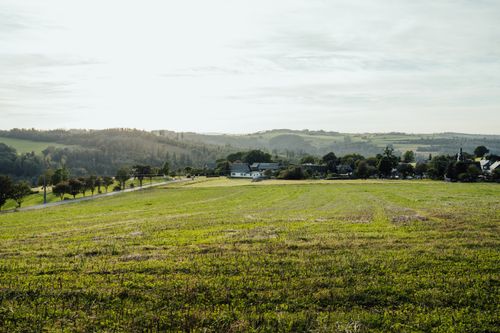 Free Tranquil countryside view of rolling hills, farmland, and a small village at sunset. Stock Photo