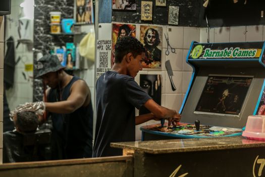 Youth playing arcade game in a lively barbershop setting capturing urban culture.