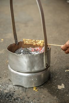 A close-up of corn being grilled over hot coals in a portable stove on a street.