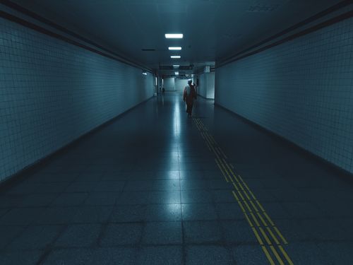Free A lone figure walks through an empty, moody underground tunnel with reflective floors. Stock Photo