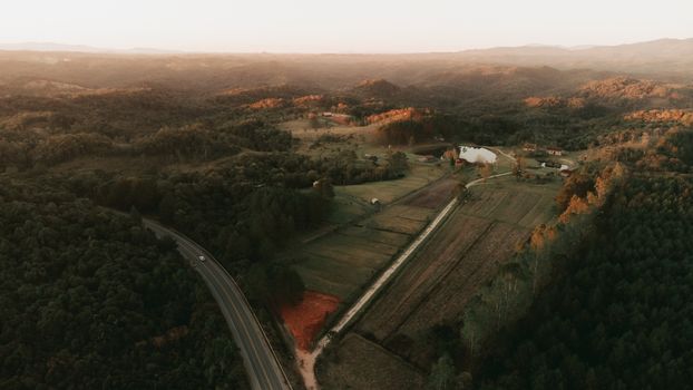 Aerial view of a scenic rural valley at sunset featuring a highway and farmland surrounded by hills.