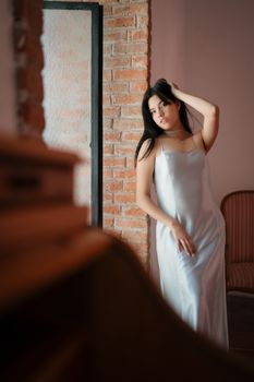 Elegant woman in a silky dress posing indoors by a brick wall in Santiago de Querétaro.