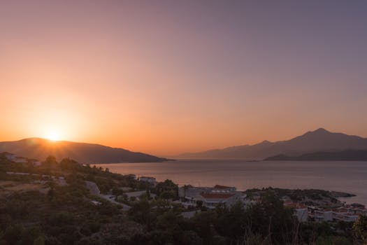 从宁静的海滨村庄俯瞰，以山脉为背景的日落景色令人惊叹，捕捉到了大自然之美的本质