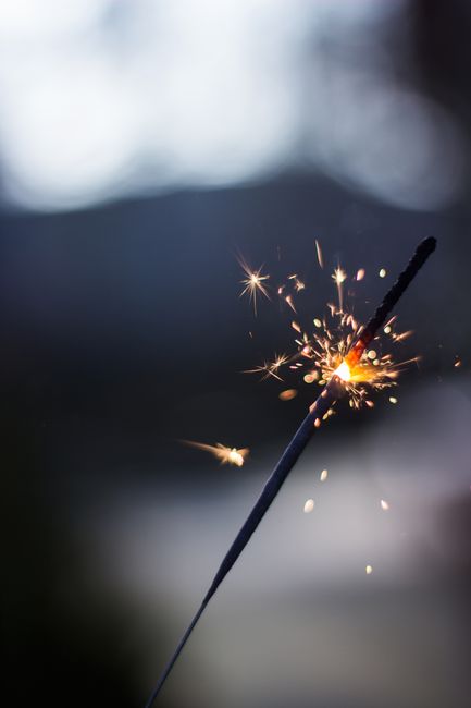 A sparkler ignites with brilliant sparks against a moody twilight background.