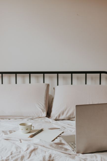 A minimalist home office setup on a bed with laptop, coffee, and notepad.
