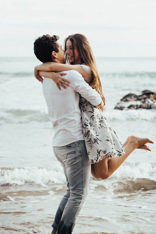 Photo of a Man Lifting Woman Near Body of Water