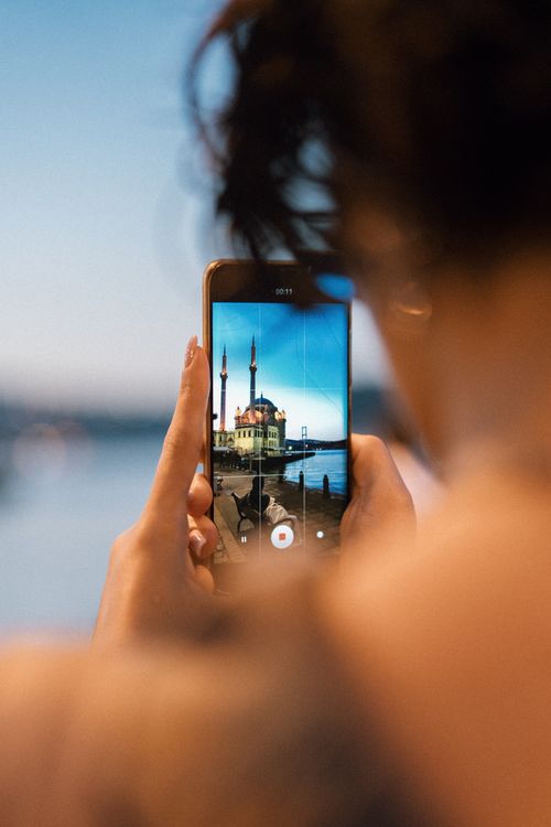 Free A person photographs Ortaköy Mosque in Istanbul with a smartphone during sunset, depicting vibrant urban culture. Stock Photo