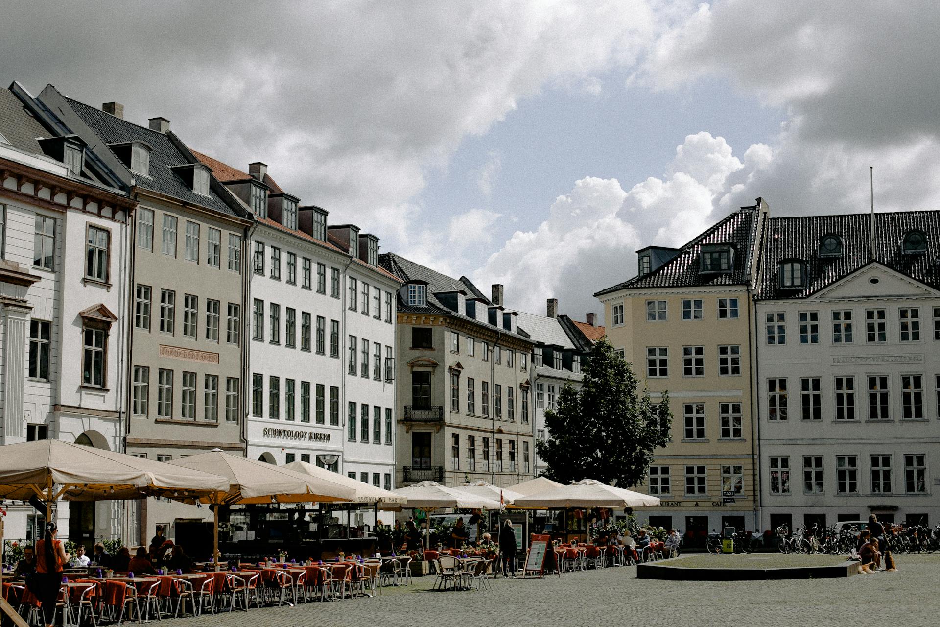 Lively European plaza with outdoor cafes, classic architecture, and people enjoying a sunny day.