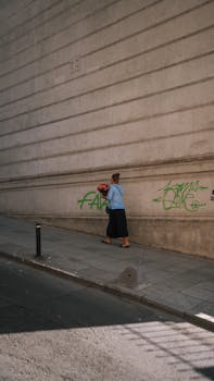 A woman in blue walks past a graffiti-covered wall carrying a bouquet.
