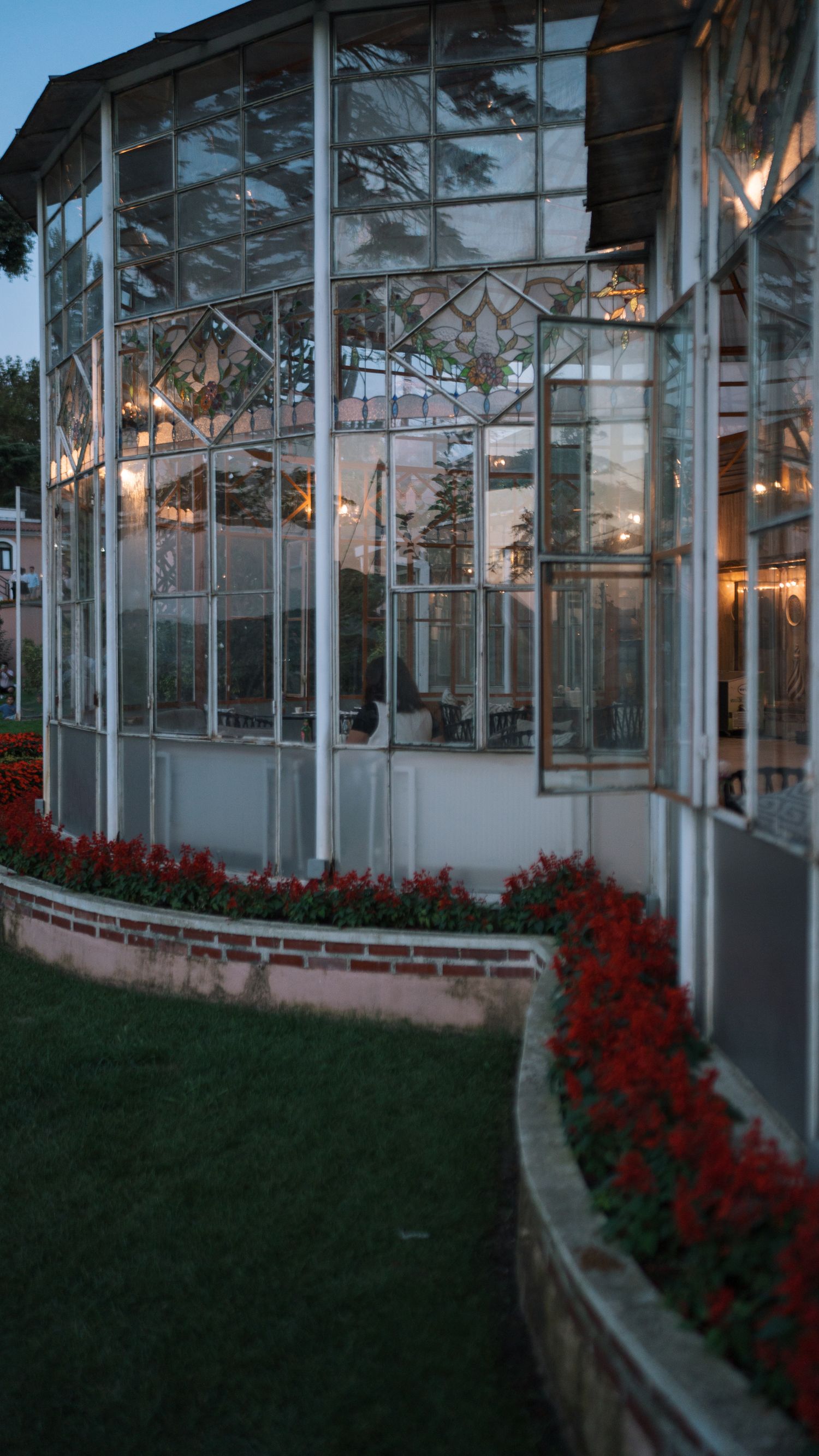 Glazed conservatory lit at dusk beside a garden border