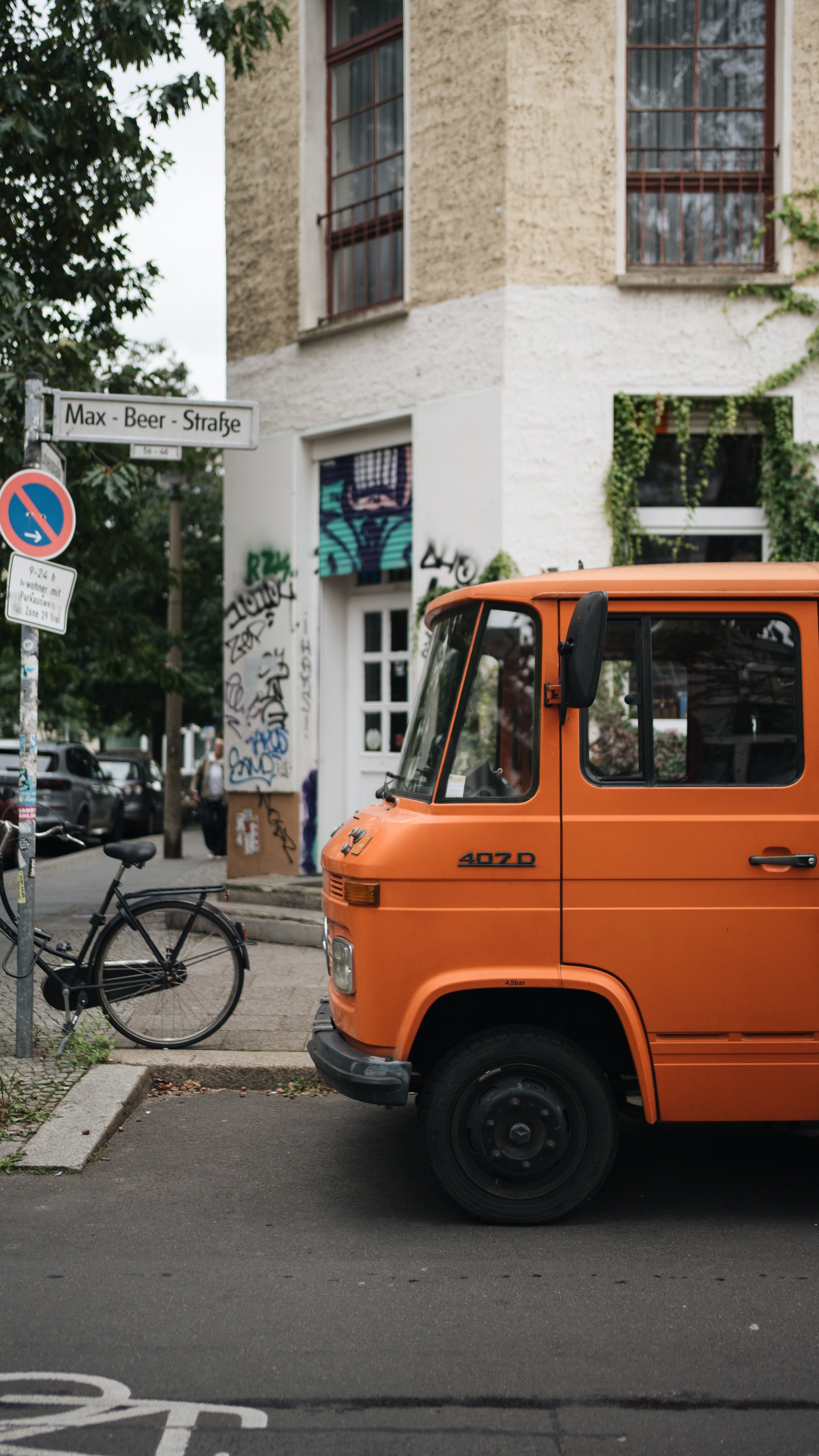 Vintage orange van parked on Max Beer Street, urban vibe with graffiti and bicycle nearby.