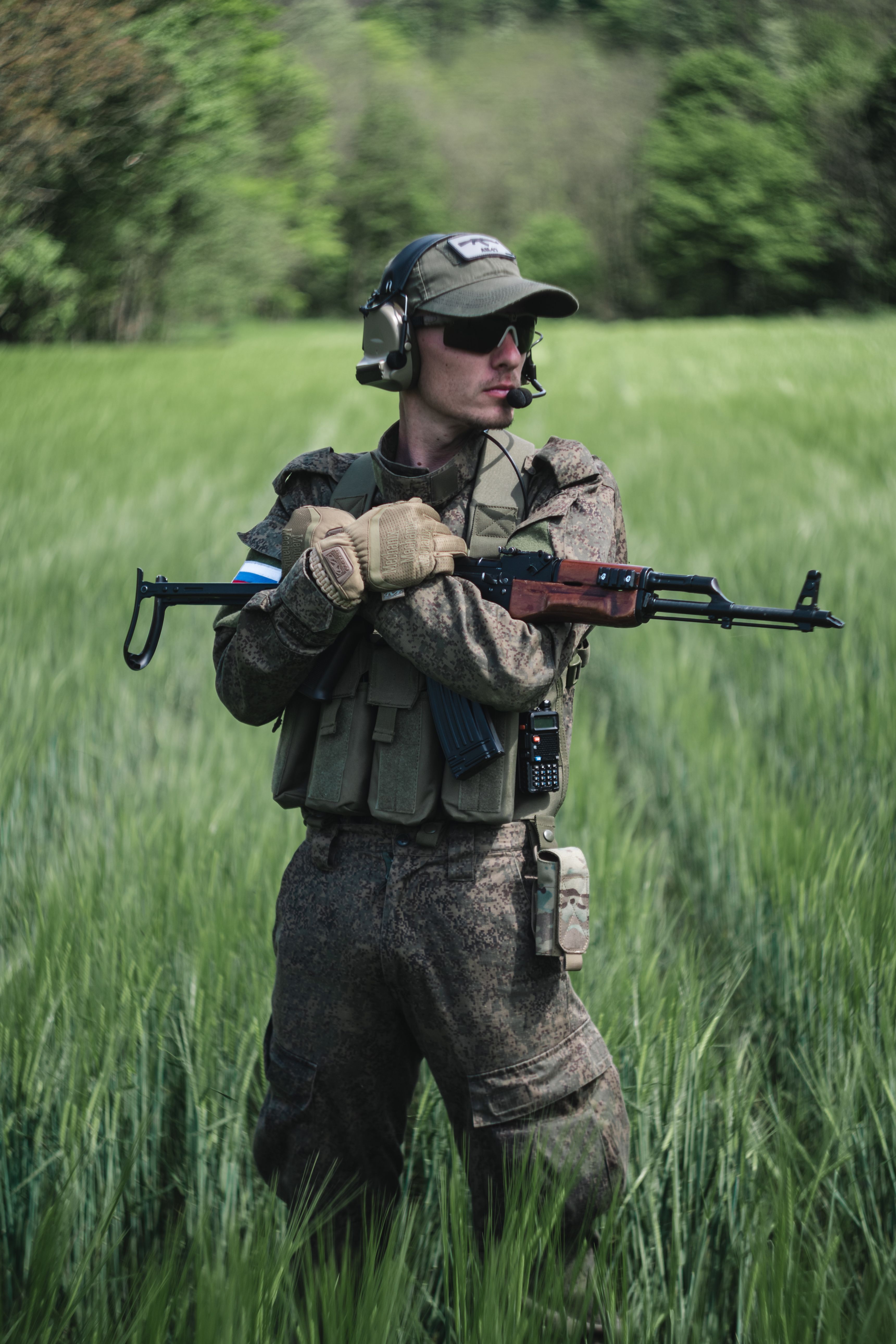 A soldier in camouflage gear stands in a grassy field holding a rifle, embodying military readiness.