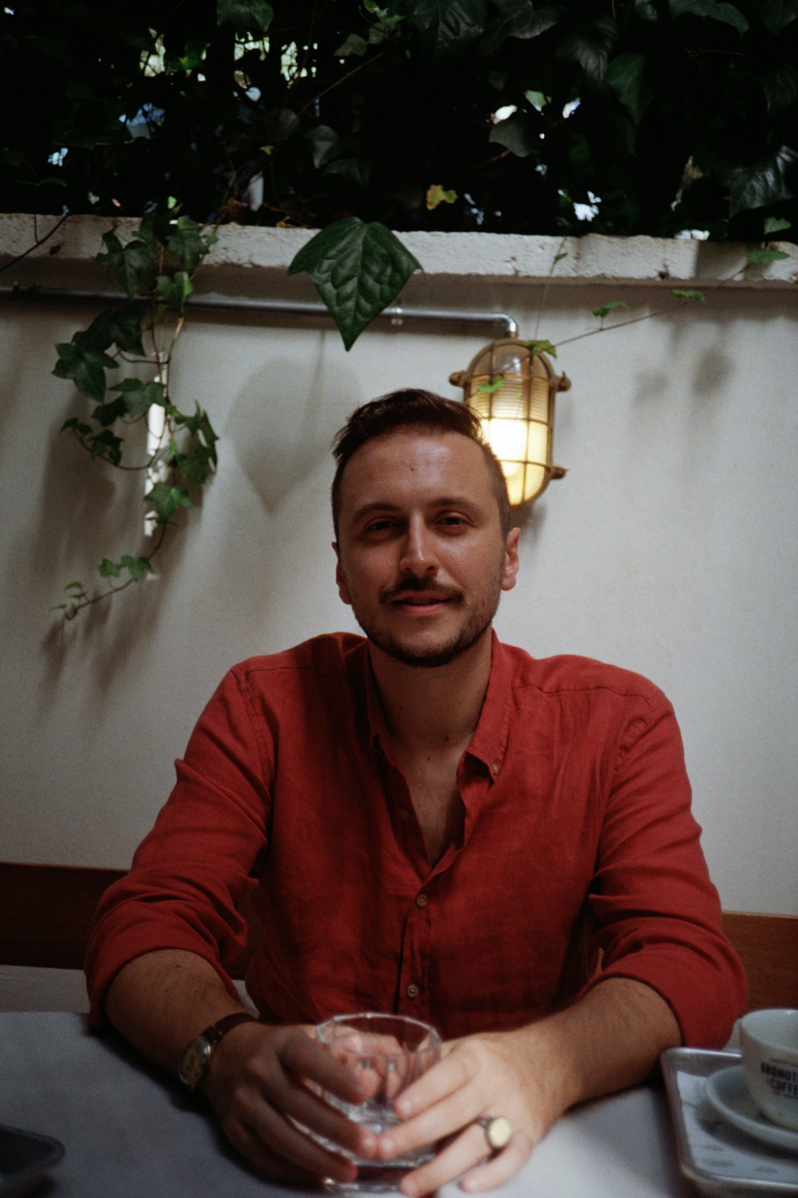 Portrait of a man in a red shirt holding a drink in a cozy indoor setting.