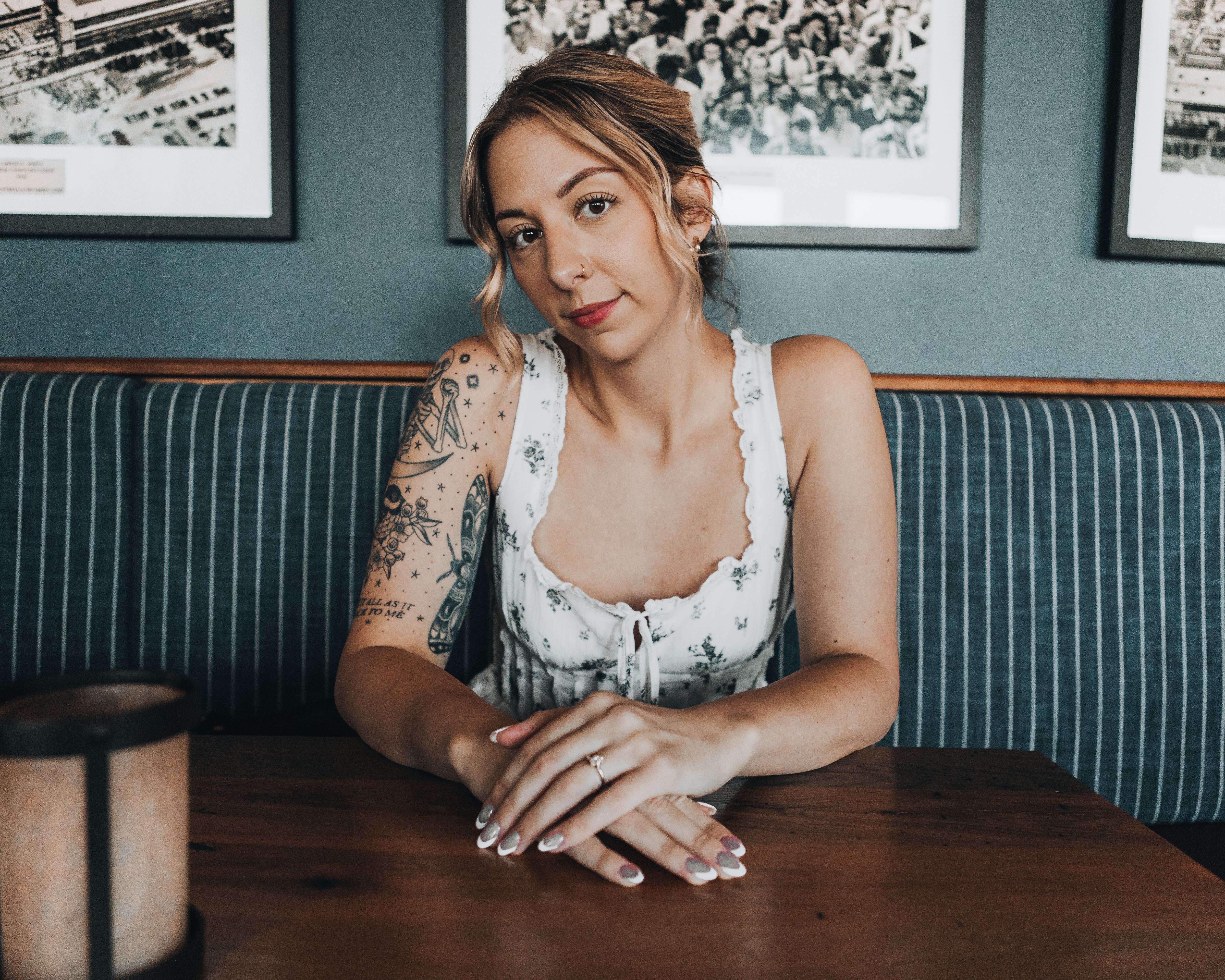 Charming woman with tattoos sitting indoors in Portland, ME, showcasing fashion and relaxation.
