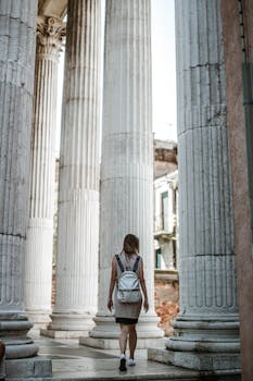 Woman walking among grand ancient stone columns in daylight, showcasing classic architectural beauty.