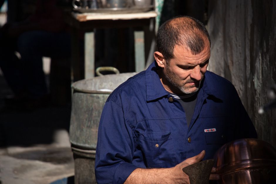 An artisan crafting metalware outdoors in Tripoli, showcasing traditional skills.