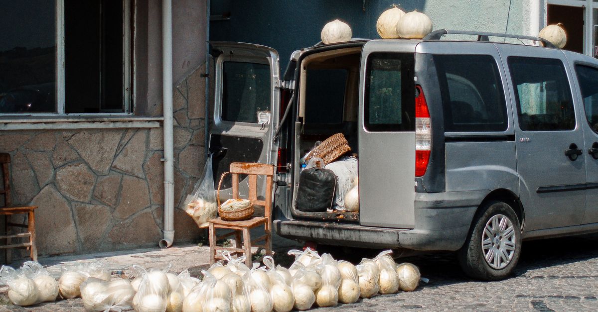 A van unloading pumpkins on a cobblestone street beside a building with open doors.