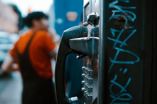 Free Close-up of a payphone with graffiti, blurred background showing a person. Stock Photo