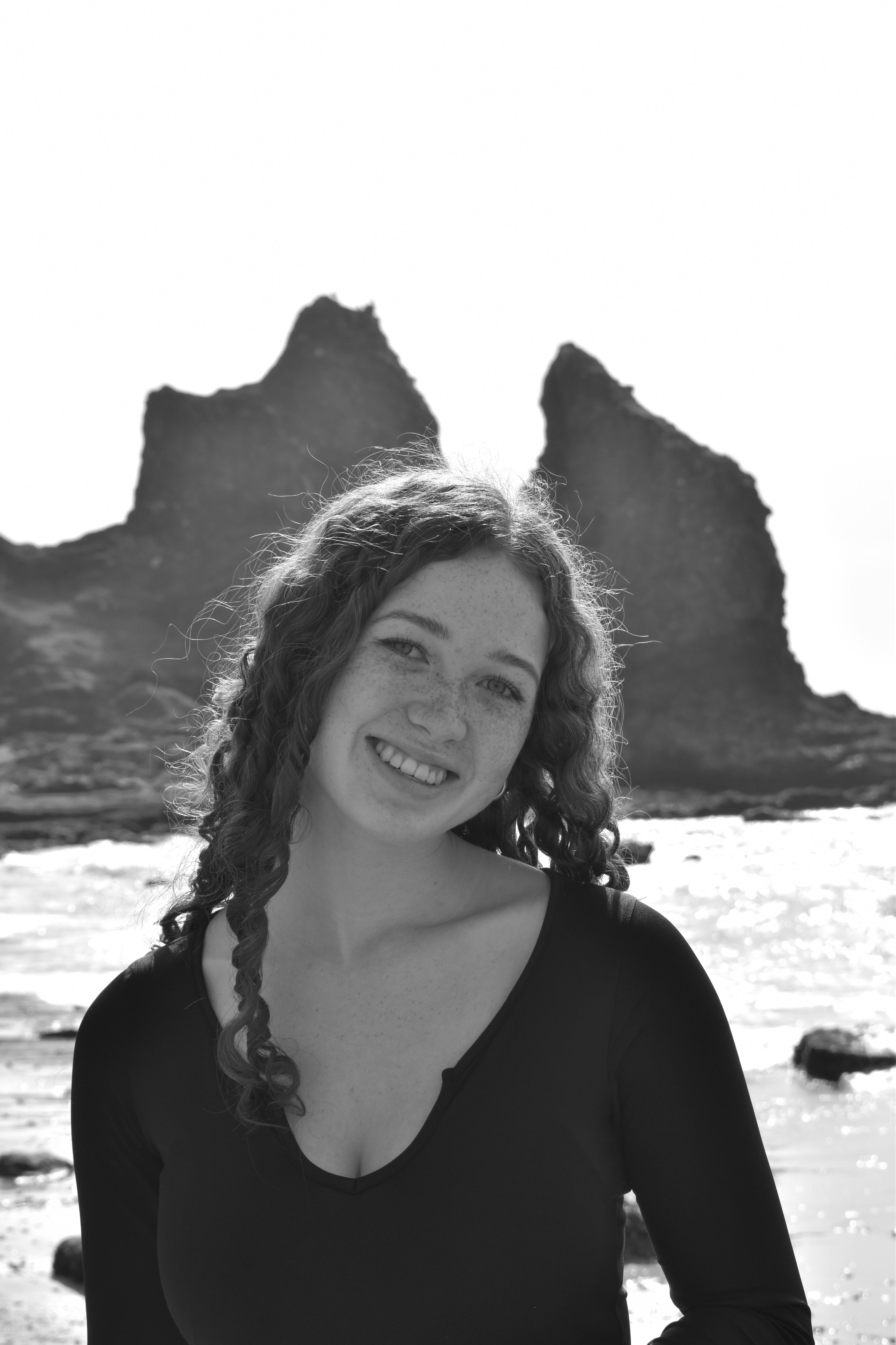 A serene portrait of a woman with curly hair by the rocky seashore in Faro, Portugal.