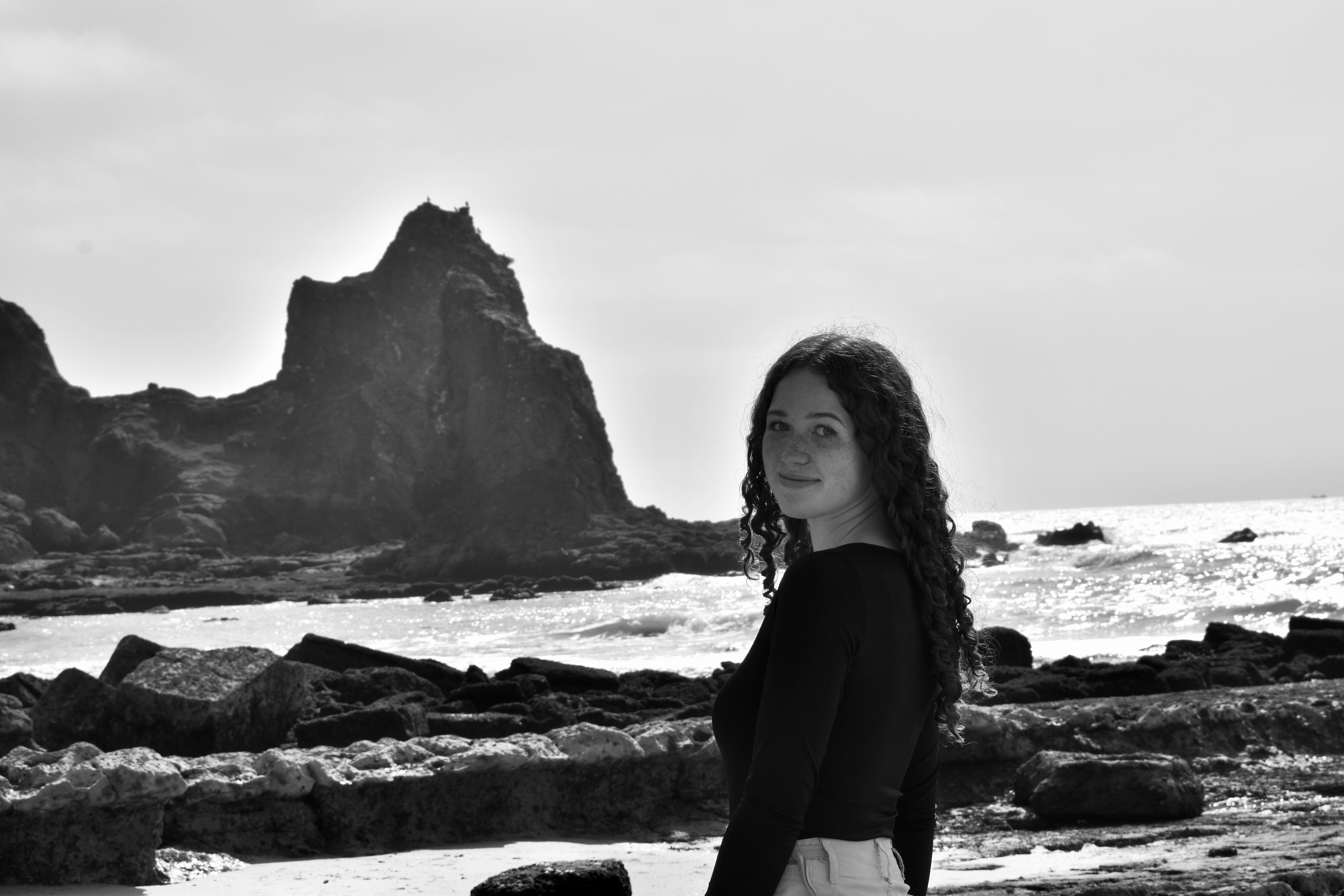 A young woman with curly hair at a rocky seashore in Faro, Portugal.
