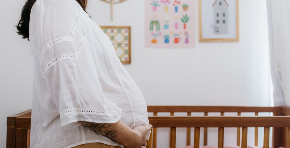A pregnant woman standing beside a wooden crib — the same household where the don't-mop-along-the-wall rule decides whether the treatment holds for the next 3 months