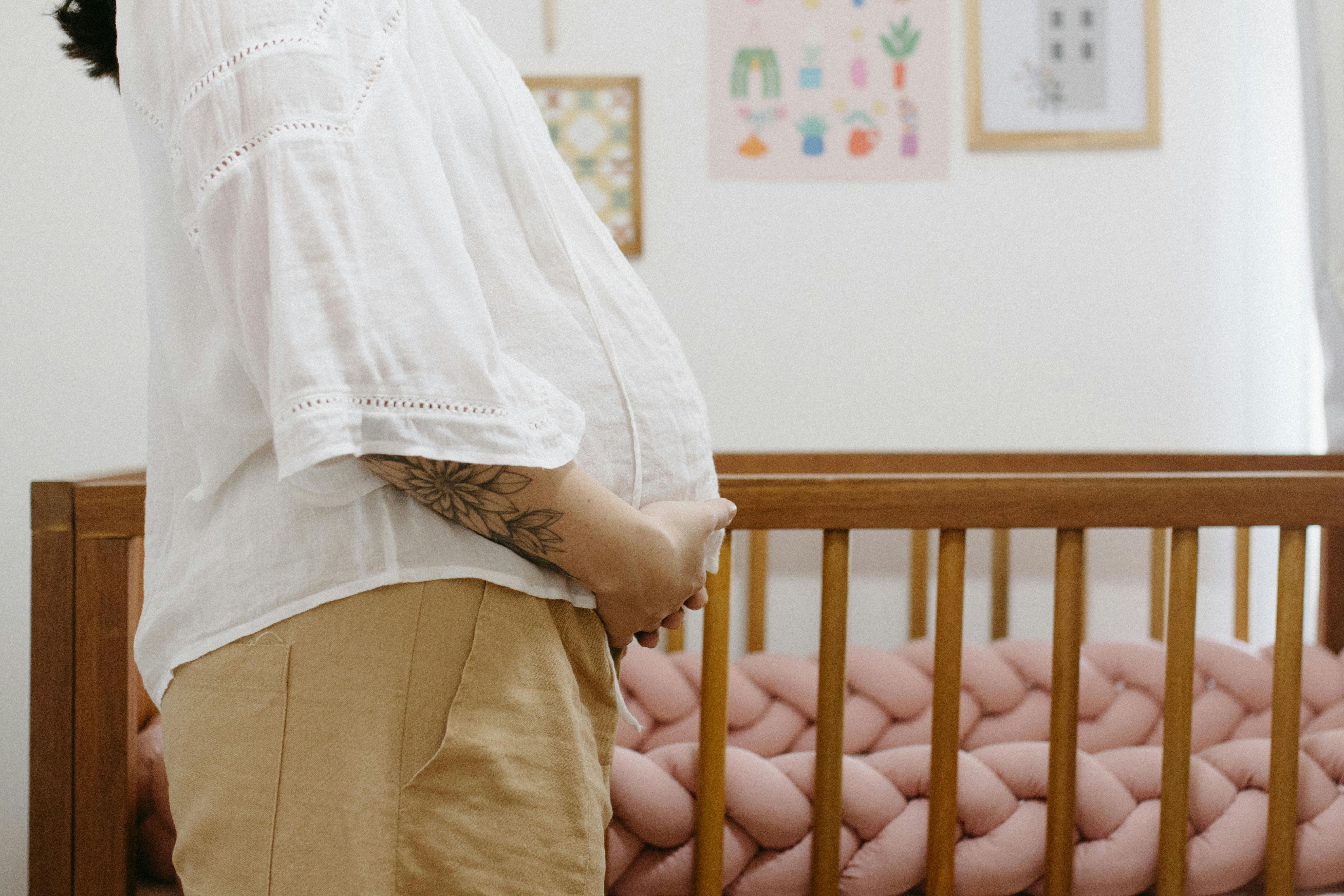 a pregnant woman stands in front of a crib