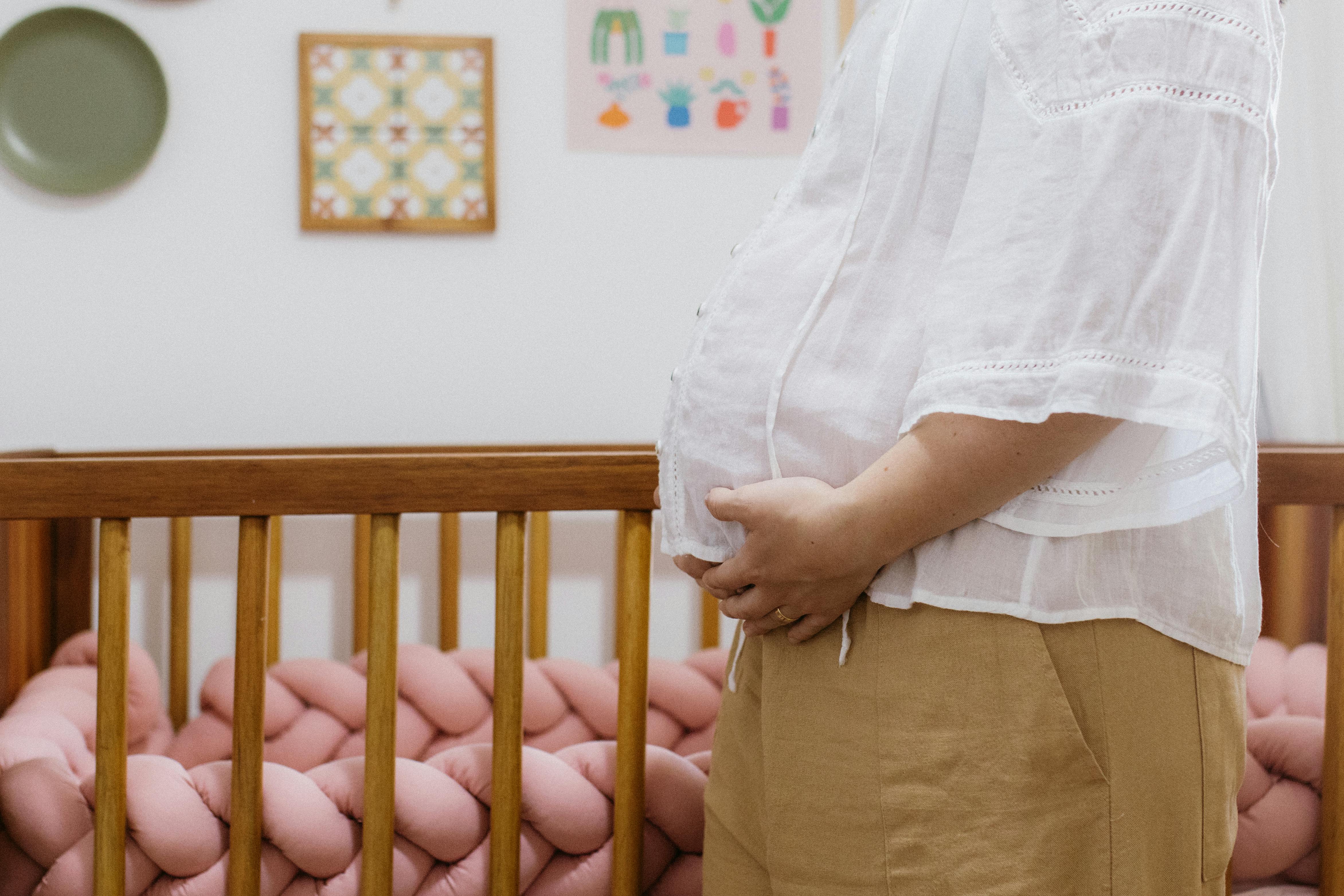 A pregnant woman standing beside a crib in a cozy nursery room.