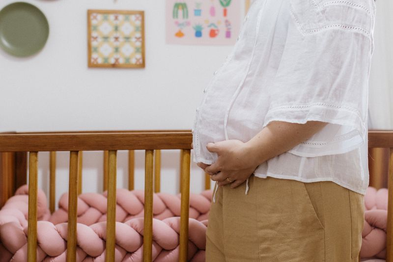 A pregnant woman standing beside a crib in a cozy nursery room.