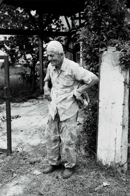 Black and white portrait of an elderly man standing outdoors in a rural setting in Sinop, Türkiye.