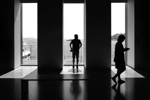 Free Silhouetted figures in a modern room with a waterfront view, creating a dramatic effect. Stock Photo