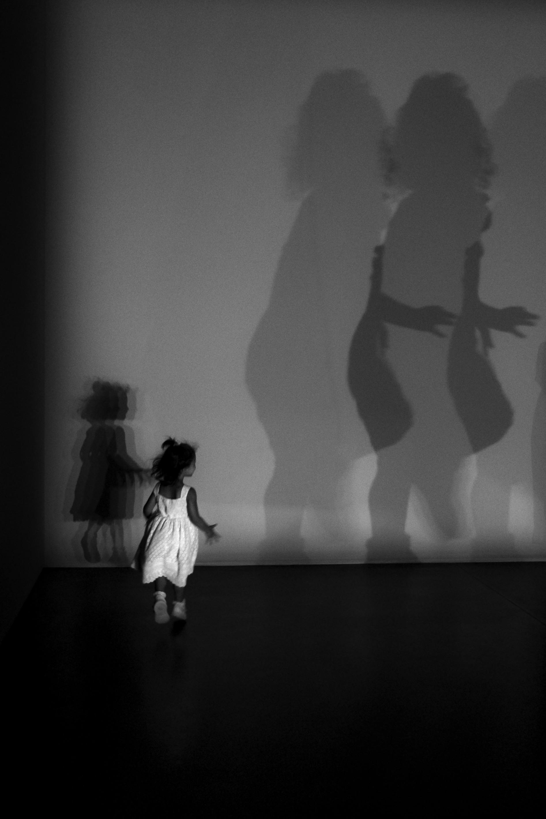 Free A child in a white dress runs towards projected shadows on a wall. Stock Photo