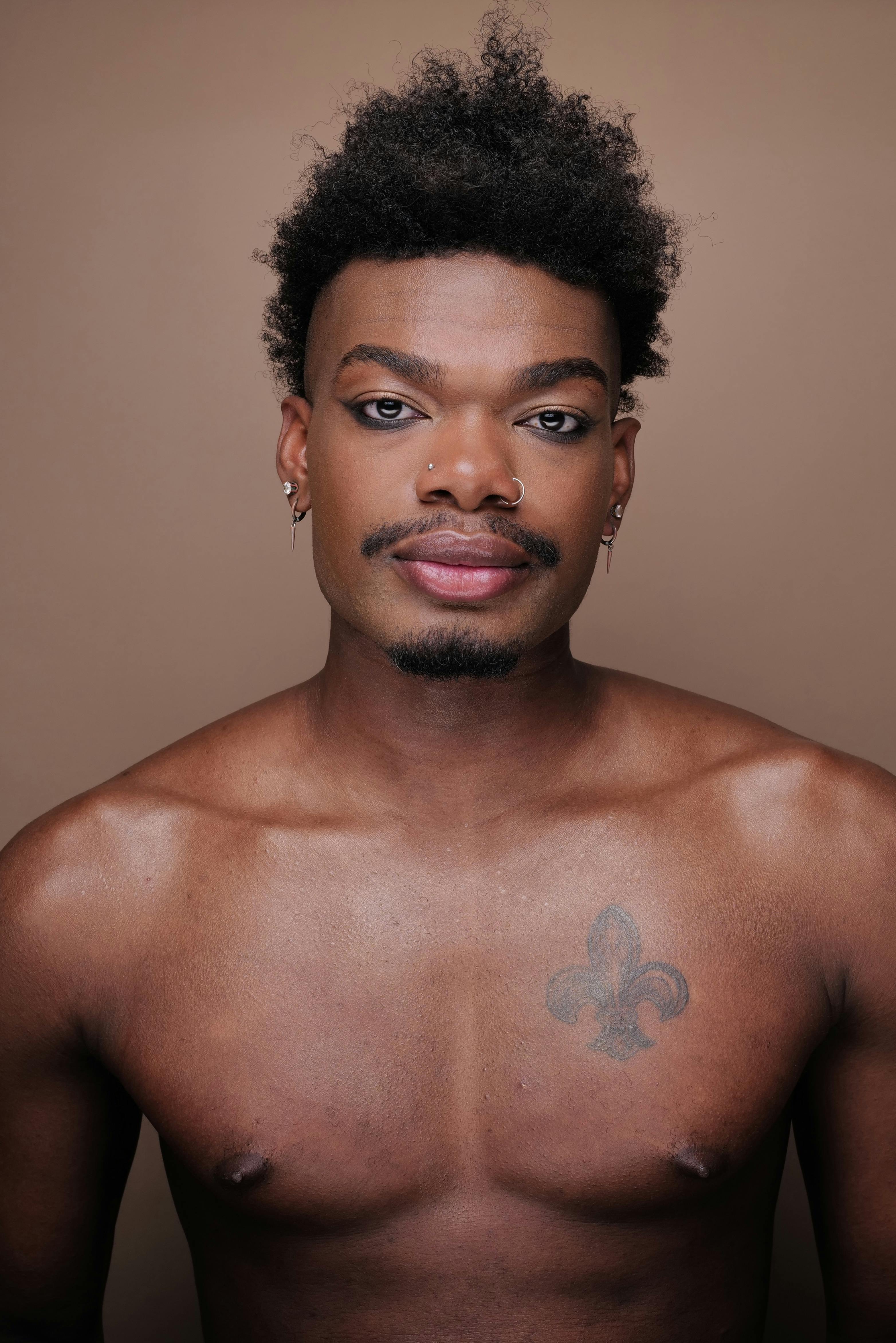 Expressive portrait of a shirtless man with tattoos in a modern studio setting, emphasizing personality and style.