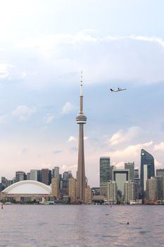 Toronto skyline featuring the CN Tower at sunset with a plane flying overhead.