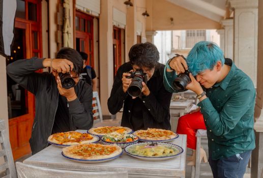 Three photographers taking pictures of a variety of pizzas at an outdoor restaurant in Lerma, Mexico.