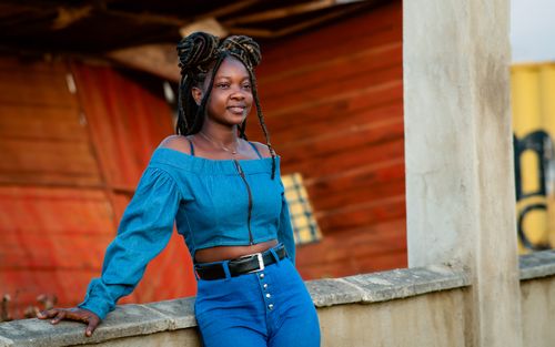 Free A woman in blue denim leaning on a concrete structure with vibrant backdrop. Stock Photo