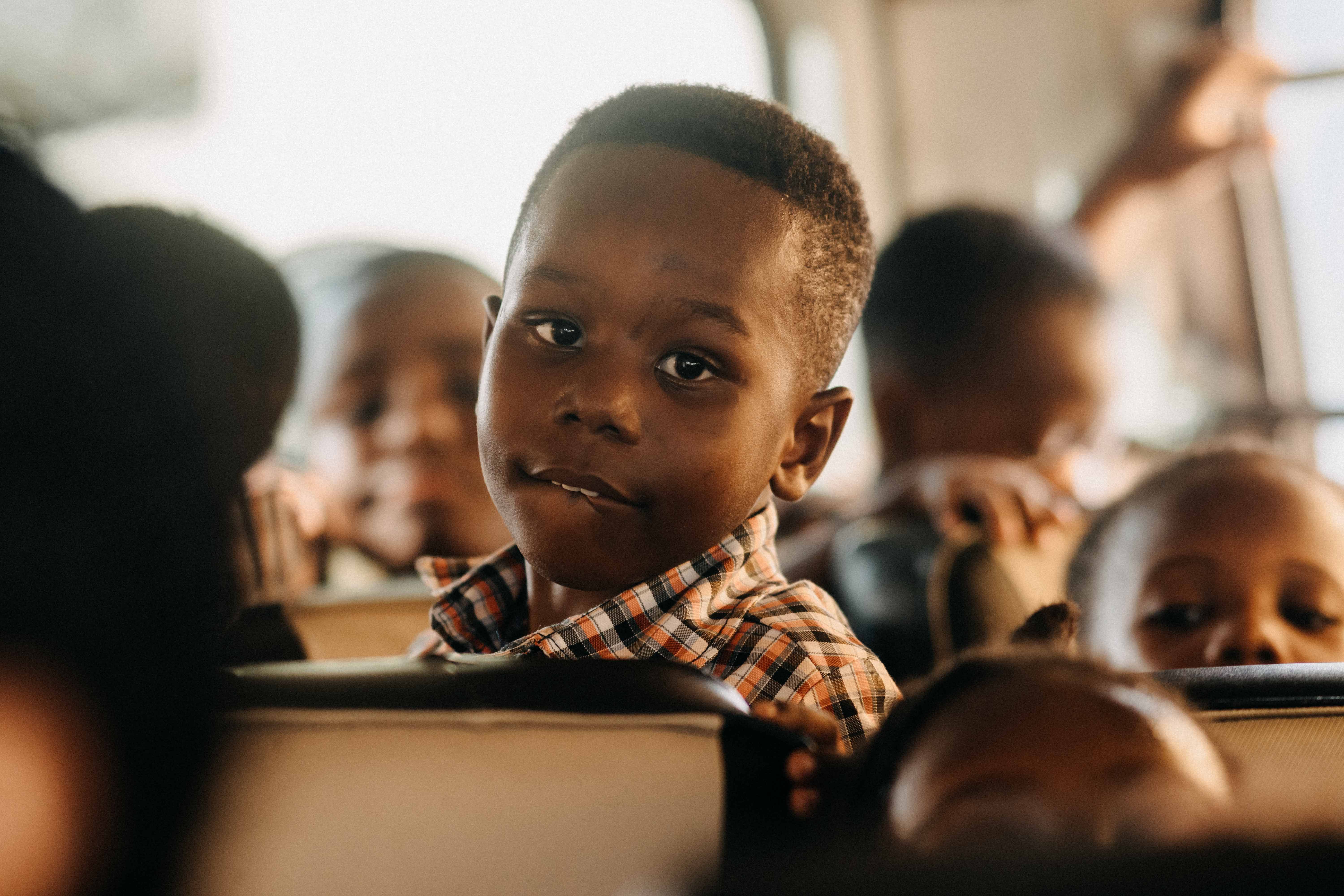 A young boy on a school bus gazes thoughtfully ahead, surrounded by other children, capturing a moment of reflection.