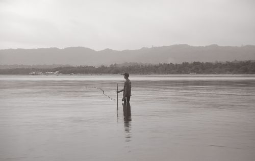 Free A lone fisherman casts his net in the calm waters of Bayawan City at dusk. Stock Photo