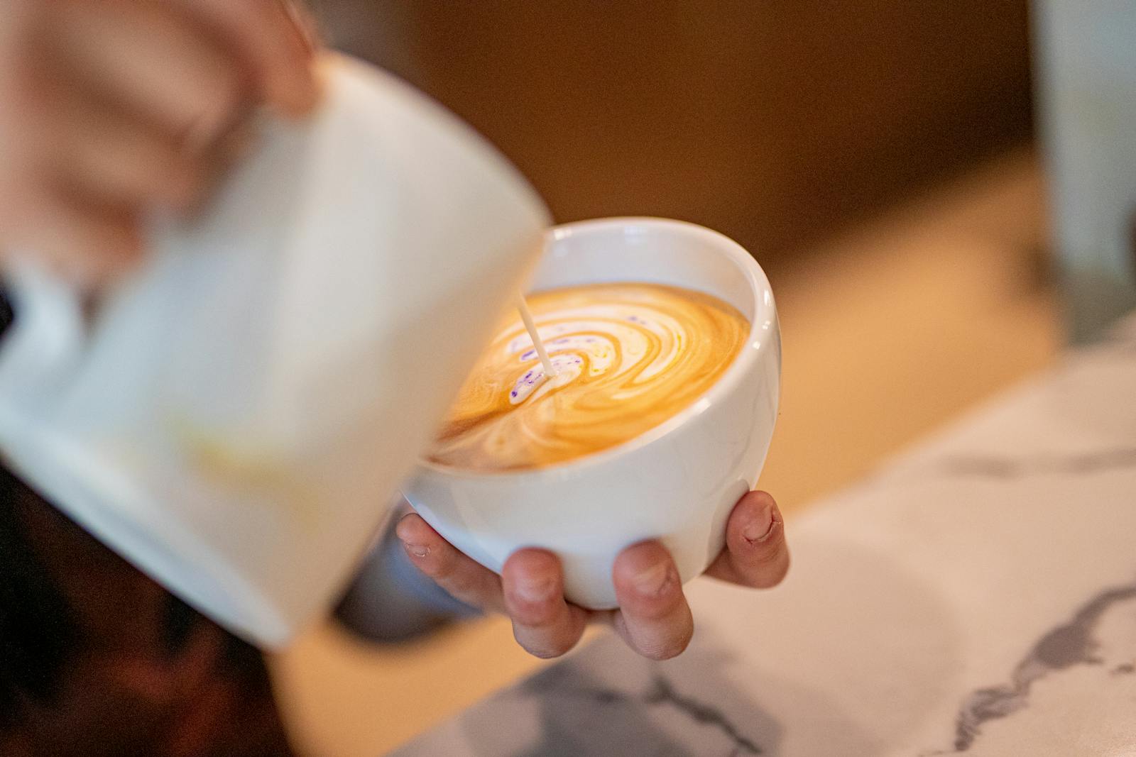 Milk being poured into espresso to form latte art in a cup