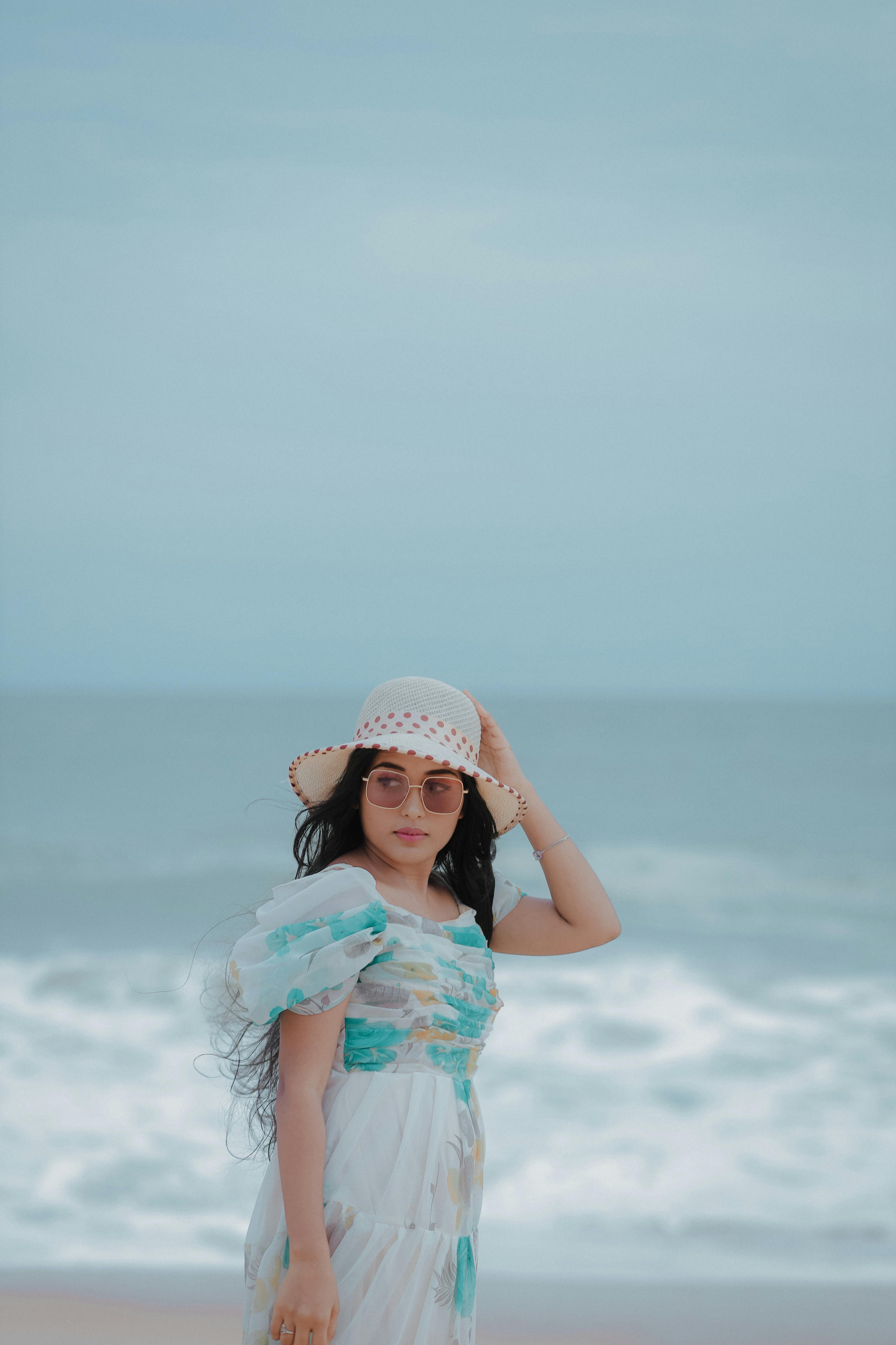 a young girl in a dress and hat standing on the beach