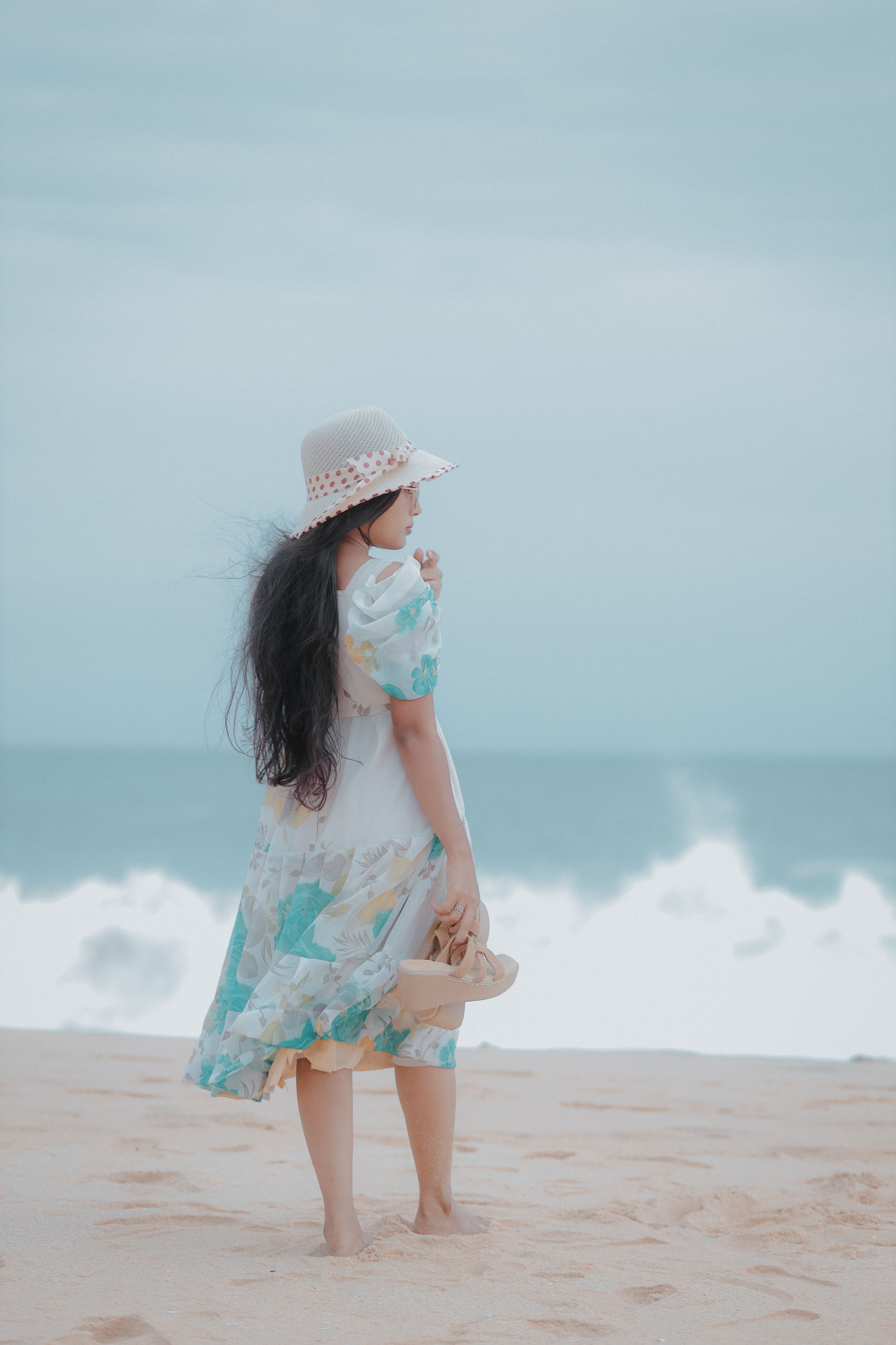 A woman in a hat and dress walking on the beach · Free Stock Photo