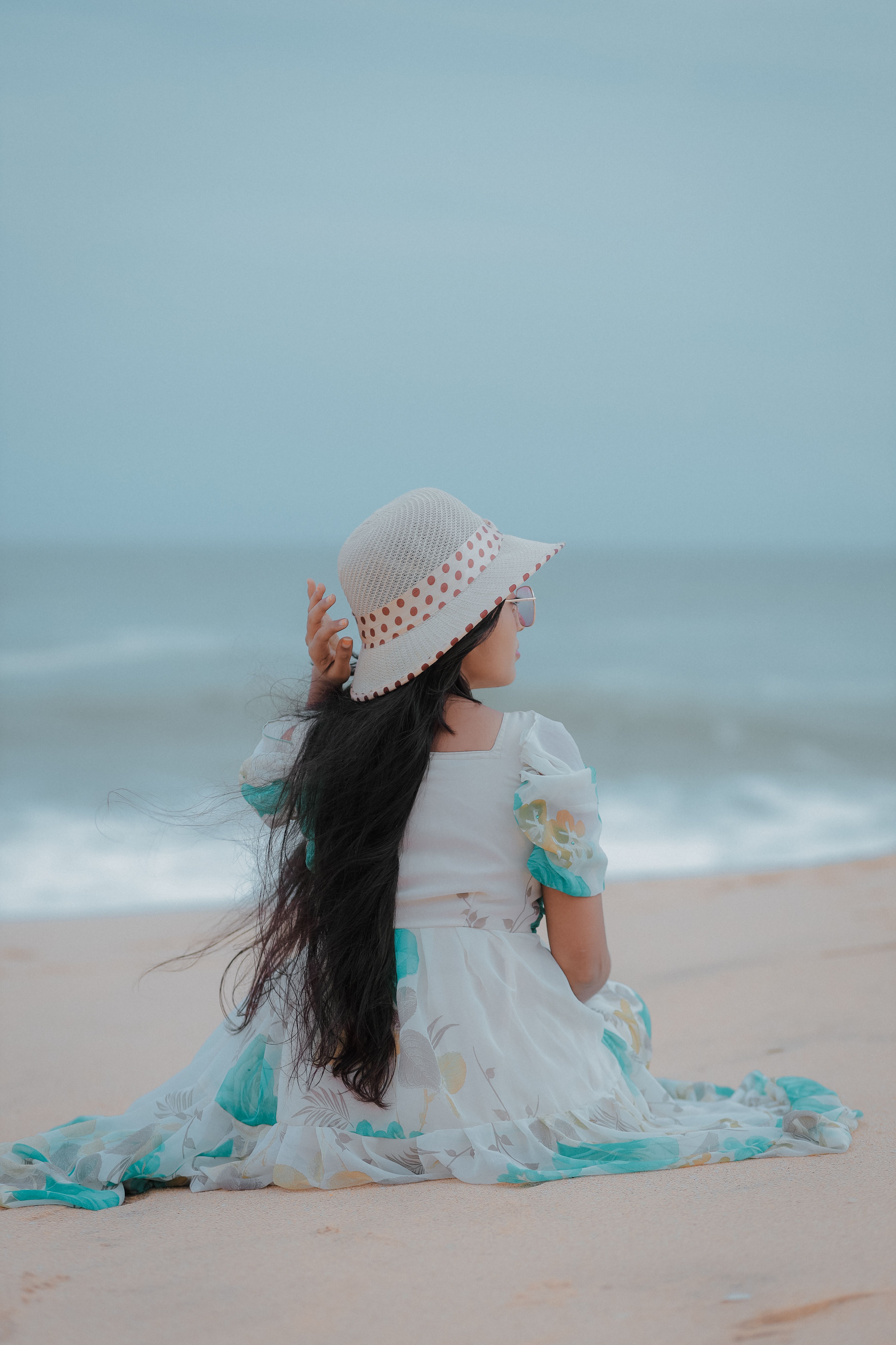 A woman sitting on the beach with a hat on · Free Stock Photo