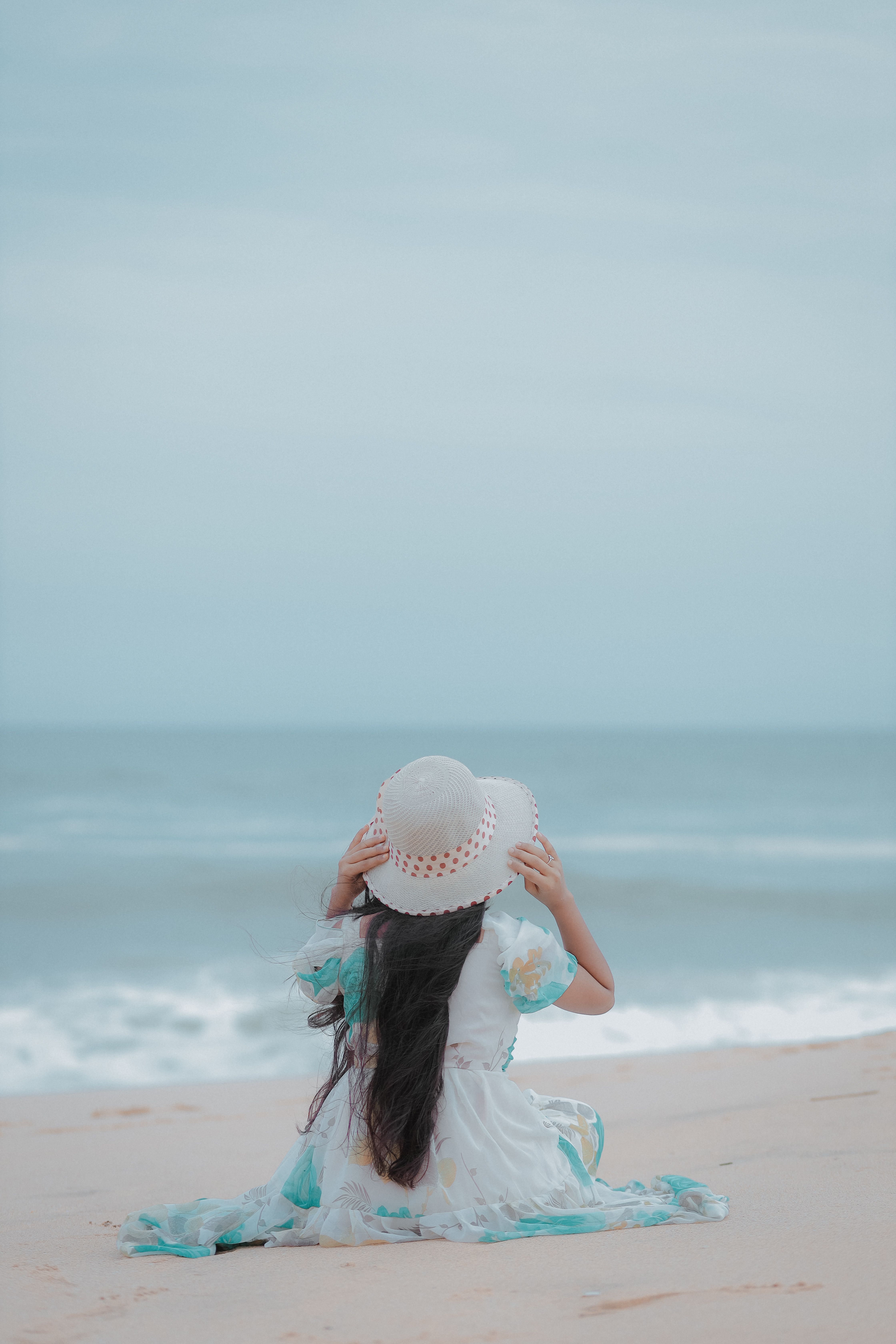 A woman sitting on the beach with her back to the ocean · Free Stock Photo