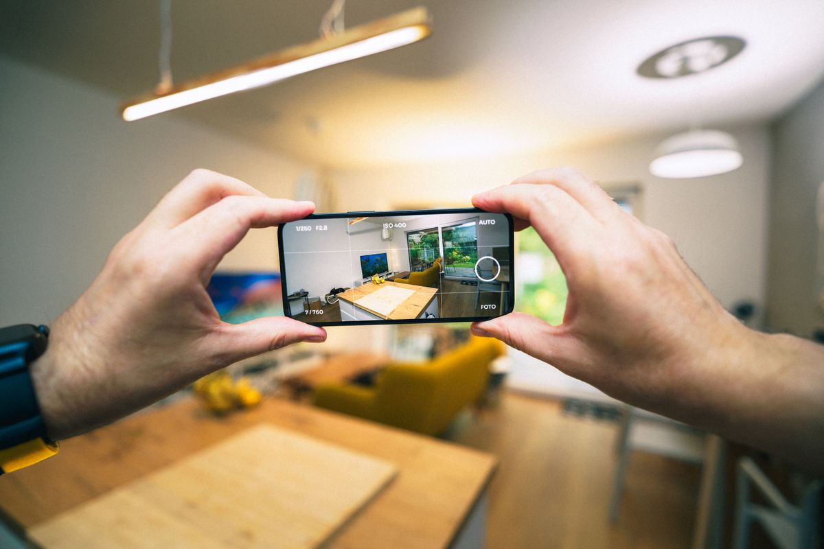 Hender som fotograferer leilighetsinteriør med smarttelefon for dokumentasjon
