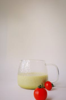Glass of creamy avocado smoothie alongside ripe cherry tomatoes on a minimalist background.