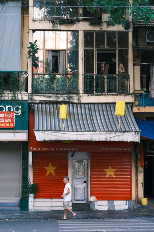 Free A man walks past a colorful urban store with Vietnamese flags in front. Stock Photo