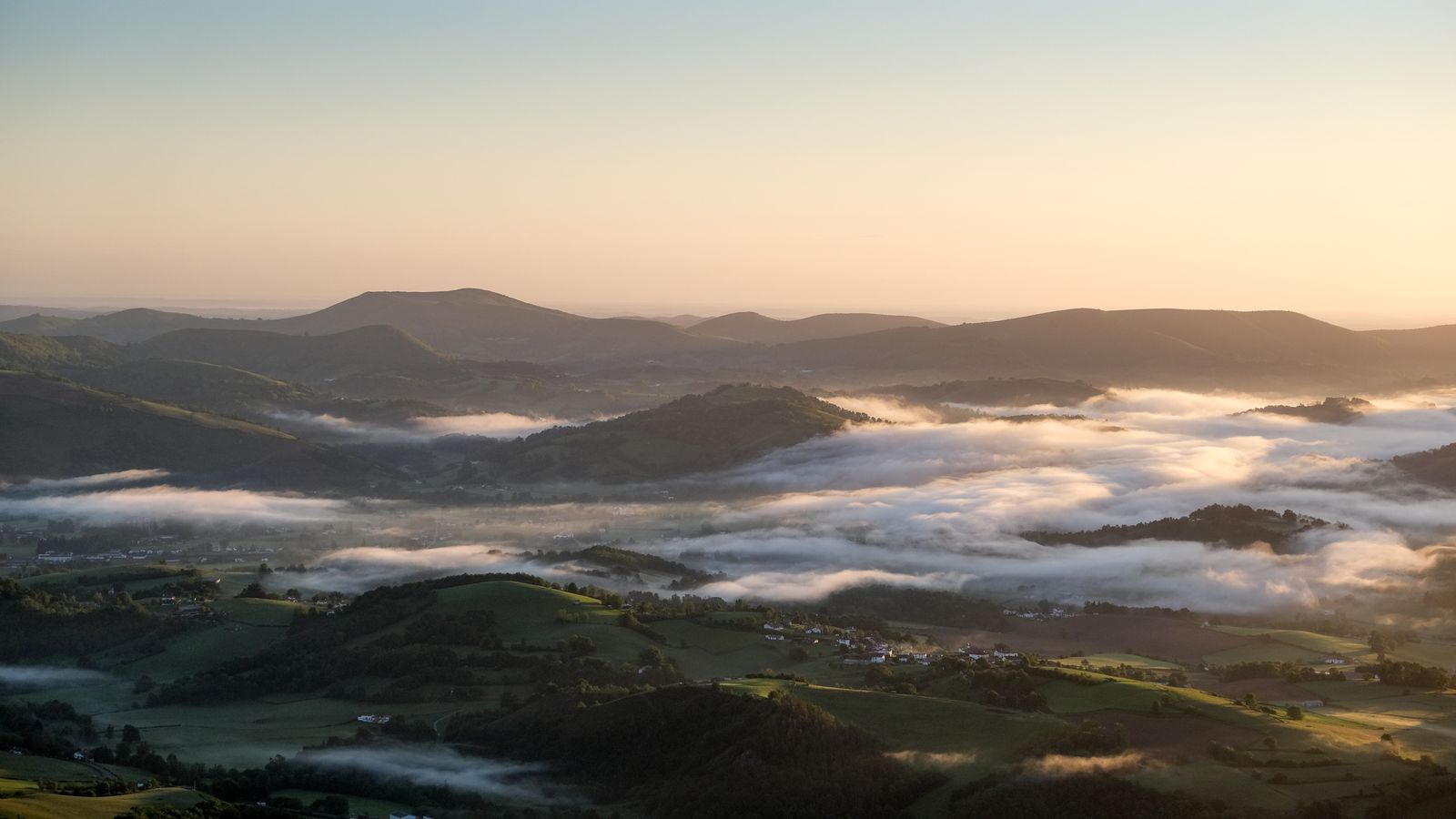 Paysage aérien du Pays Basque avec maisons aux toits de tuiles, champs et routes sous une lumière douce et couverte
