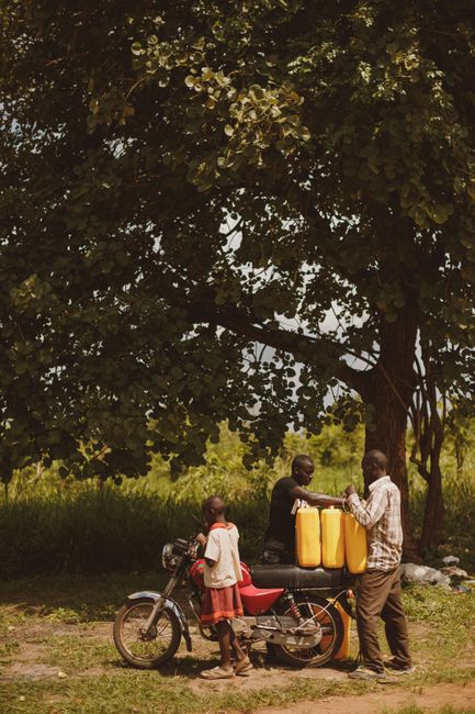 Men and child gathering with water jugs near a motorcycle in Orom, Uganda.